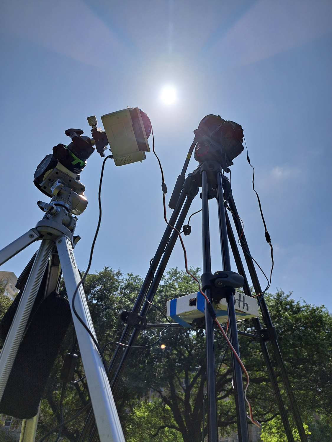 Two tripods and cameras pointed towards the sun against clear blue skies.